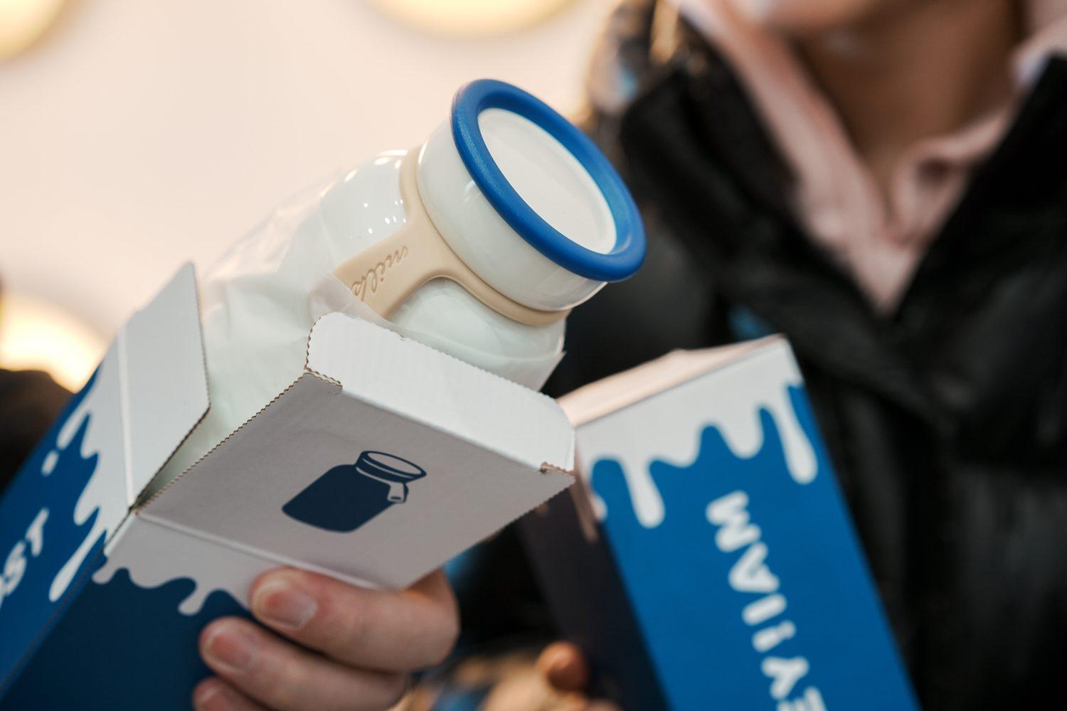A white yogurt bottle with a blue collar inside a carrier box